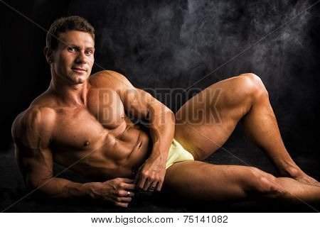 Handsome Shirtless Muscular Man Laying Down On The Floor In Bathing Suit