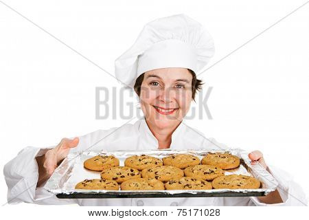 Cute female chef in her uniform, holding up a tray of delicious, freshly baked chocolate chip cookies.  Isolated on white background.  