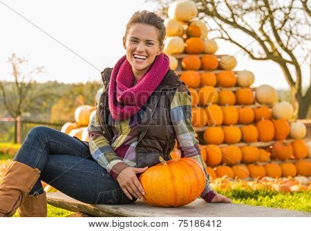 Portrait Of Happy Young Woman Sitting With Pumpkin In Front Of P