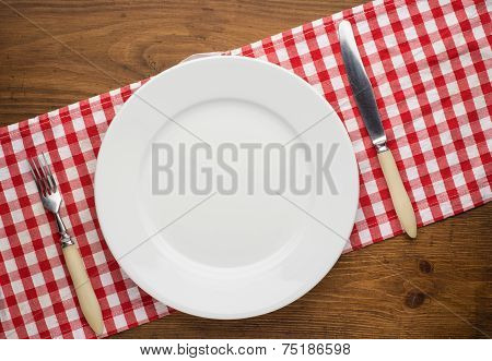 Empty plate with fork and knife on tablecloth over wooden
