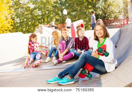 Girl with skateboard and her mates sitting