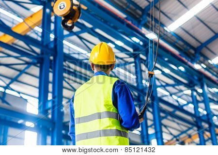 Worker in factory controlling crane with remote