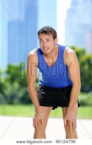 Tired man runner exhausted after sport exercise. Male jogger catching breath sweating after run workout in summer with urban background in Central Park, New York City, Manhattan, United States, USA