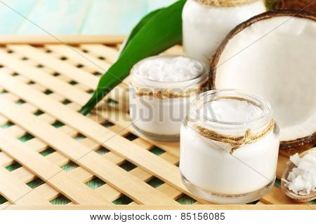 Fresh coconut oil in glassware on color wooden table and grid tray background