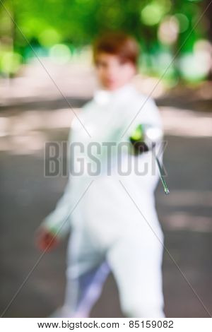 Tip of rapier held by fencer woman staying in park alley, shallow depth of field