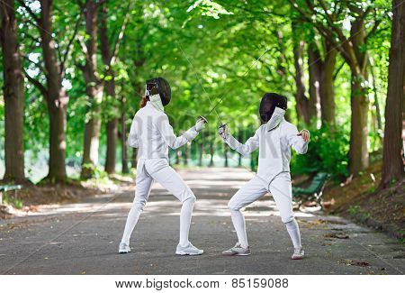 Two rapier fencers women staying in park alley getting ready for competition