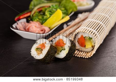 Delicious sushi rolls served on black plate and stone