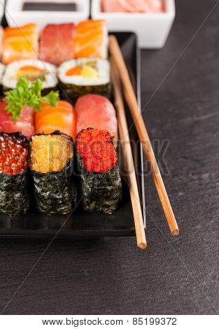 Delicious sushi rolls served on black plate and stone