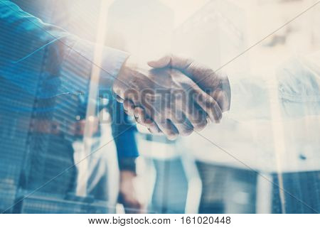 Double exposure concept.Close up view of business partnership handshake concept.Photo two businessman handshaking process.Skyscraper office building on the blurred background.Horizontal, flares effect