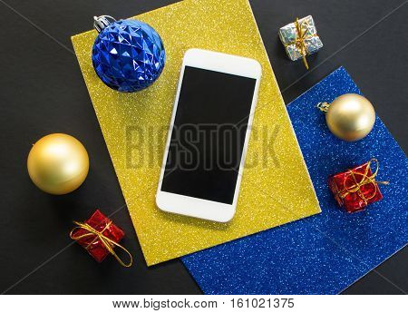 Christmas tree ornament and smartphone flat composition. White smartphone with black screen on table. Christmas or New Year mockup with personal gadget. Smartphone top view with winter holiday decor