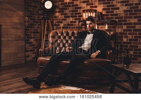 Young Man In Suit Resting On Sofa With Glass Of Brendy After Working Day