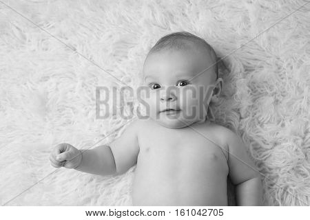 A black and white portrait of a baby boy lying on a flokati rug.