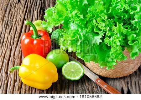 The salad in basket, sweet pepper, half leech lime, lemon, apple and kitchen knife put on the bark.