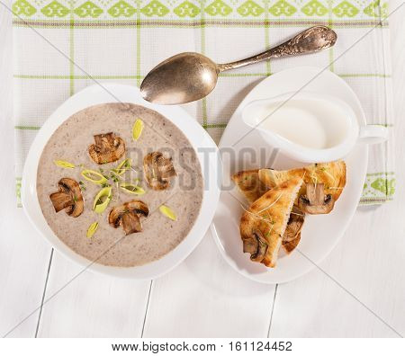 Soup with champignons leek and crispy croutons on white background top view.
