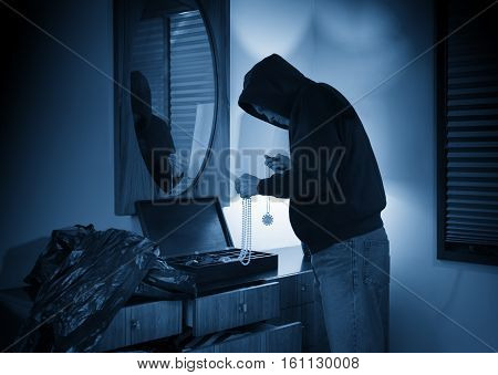 Hooded burglar ransacking a jewelry box in a home