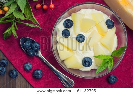 Curd with melon, blueberries and a sprig of mint. Wooden background