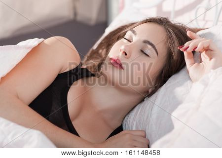 Beautiful girl sleeping in bed early in morning. Portrait of young beautiful woman having rest in her bed. Drunk dream, sleeping pill, exhaustion, tiredness concept