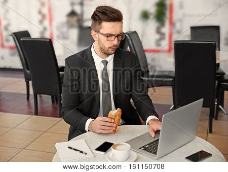 Young businessman having snack while working with laptop in cafe