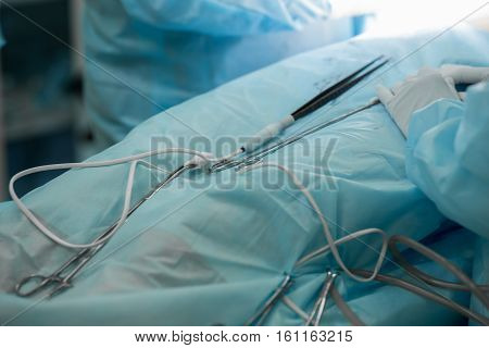 Close-up image of surgical instruments during cosmetic surgery on breasts. Forceps and tweezers doctor operating a patient. Plastic surgery breast augmentation enlargement enhancement. Hands of a surgical team during surgery.