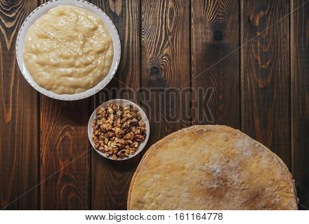 Ingredients for baking a cake, top view on wooden board. shortcakes, buttercream or cream and nuts on a plate on vintage wooden kitchen table. copyspace for cook recipe.