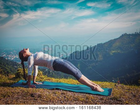 Woman doing Hatha yoga asana Purvottanasana plank pose  outdoors in mountains. Vintage retro effect filtered hipster style image.