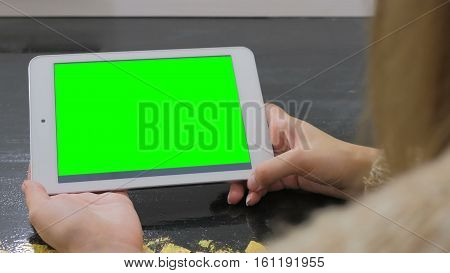 Woman looking at horizontal tablet computer with green screen. Close up shot of woman's hands with pad