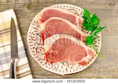 A white plate of raw sliced meat on wooden table top view. Food a knife branches of greens