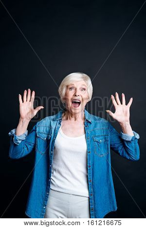 Emotionaly charged. Positive smiling elderly woman expressing joy and holding her hands up while feeling delighted