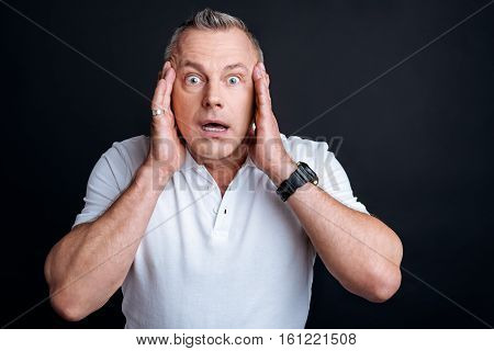 I wont believe it. Pleasant emotional man holding hands on the face and expressing wonder