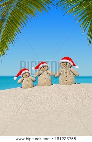 Positive sandy Snowmen family in red Santa hats at sunny ocean tropical palm beach. Happy New Year and Merry Christmas concept for hot travel destinations. Vertical natural background.