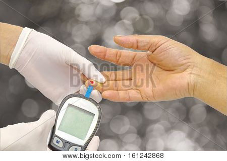 Hand of doctor checking for blood glucose meter, the blood sugar value is measured on a finger and Light bokeh background.