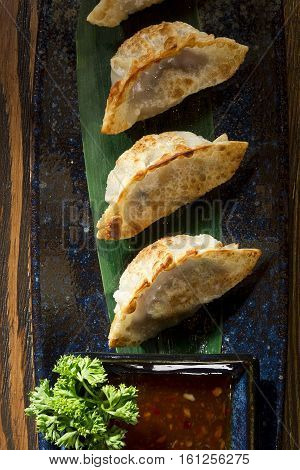 Yaki gedza with sauce in a ceramic pot on a wooden table