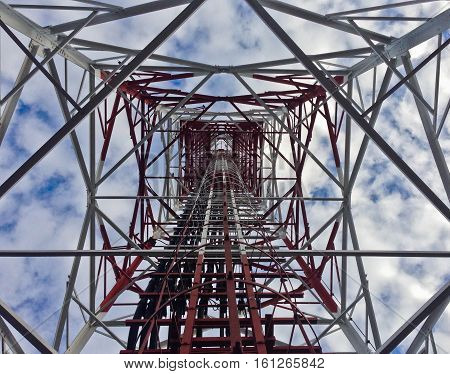 Red white telecommunication tower against blue sky and white cloud- bottom view