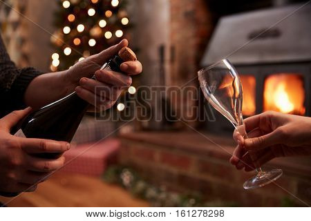 Couple Opening Champagne In Room Decorated For Christmas