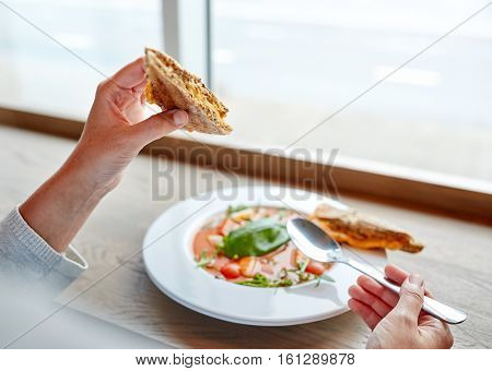 food, dinner, culinary and people concept - woman eating gazpacho soup with sandwich and spoon at restaurant