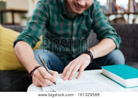 Cropped image of man in green shirt sitting on sofa by the table with book writing in notebook in office. Coworking