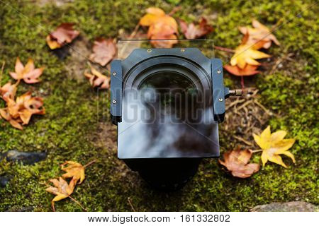 Lense with holder and graduated ND filter with autumn foliage on the yard. This filter uses for landscape photography.