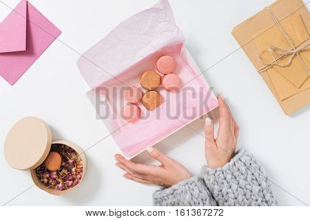 Favourite dessert. Nice young woman sitting at the table and holding a box with tasty sweet macaroons