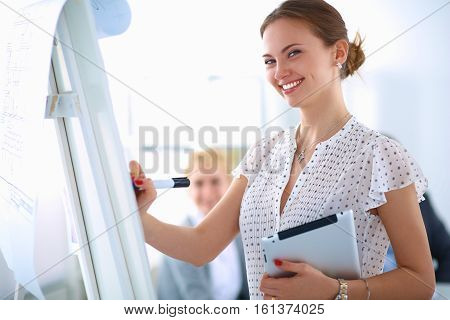 Businesswoman writing on flipchart while giving presentation to colleagues in office .
