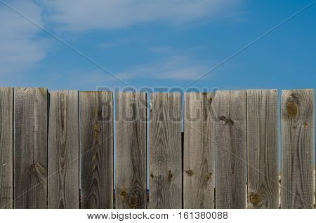 old wooden fence with gate on sky background with clouds