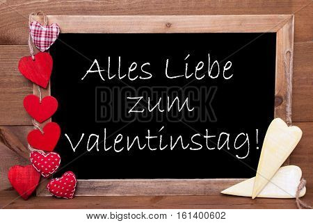 Chalkboard With German Text Alles Liebe Zum Valentinstag Means Happy Valentines Day. Red Textile And Wooden Yellow Hearts. Wooden Background With Vintage, Rustic Or Retro Style.