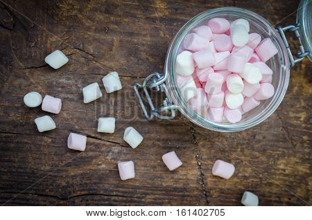 Pink and white mini marshmallows in a jar on an old rustic wooden table with space for text. Mini white and pink puffy marshmallows. Marshmallow concept. Copy space. Top view.
