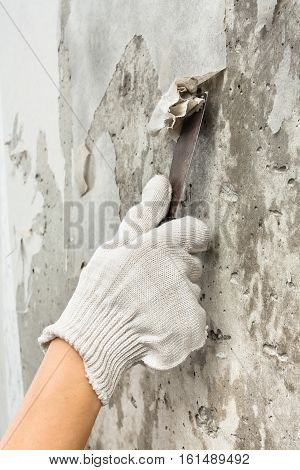 hand in gloves scraping off old wet wallpaper with spatula