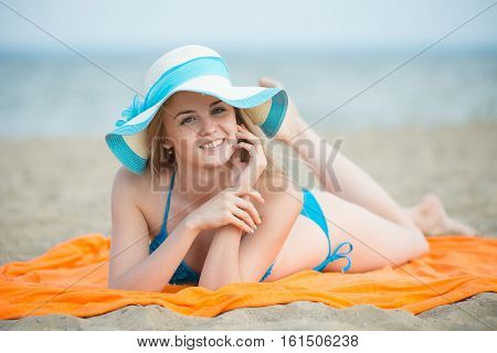 Young lady sunbathing on a beach. Beautiful woman posing at the summer sand beach. Outdoor summer portrait of pretty sport style woman in blue bikini. Ocean sea coast. Beautiful fit tan girl. Sexy slim model caucasian ethnicity outdoors.