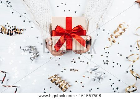 Female hands withbeautiful manicure holding present with red bow on white rustic sparkling background. Festive backdrop for holidays: Birthday, Valentines day, Christmas, New Year. Flat lay style