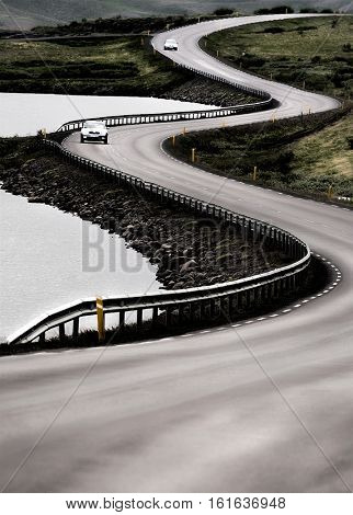 A winding road next a lake with two grey cars. Large copy-space at the bottom. Road n.1, north Iceland, Europe.