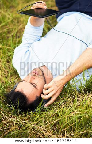 Business man lying on the green grass listen music relax with device and headphones. Upper view