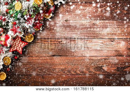 Merry Christmas Frame with Snow and wood green pine, colorful baubles, knots with berries,stars, orangesand other seasonal stuff over an old wooden aged background