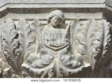 Medieval scribe or copyist writing on a book relief on doge palace capital in Venice