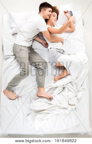 The young lovely couple lying in a bed with phone, love lconcept, top view